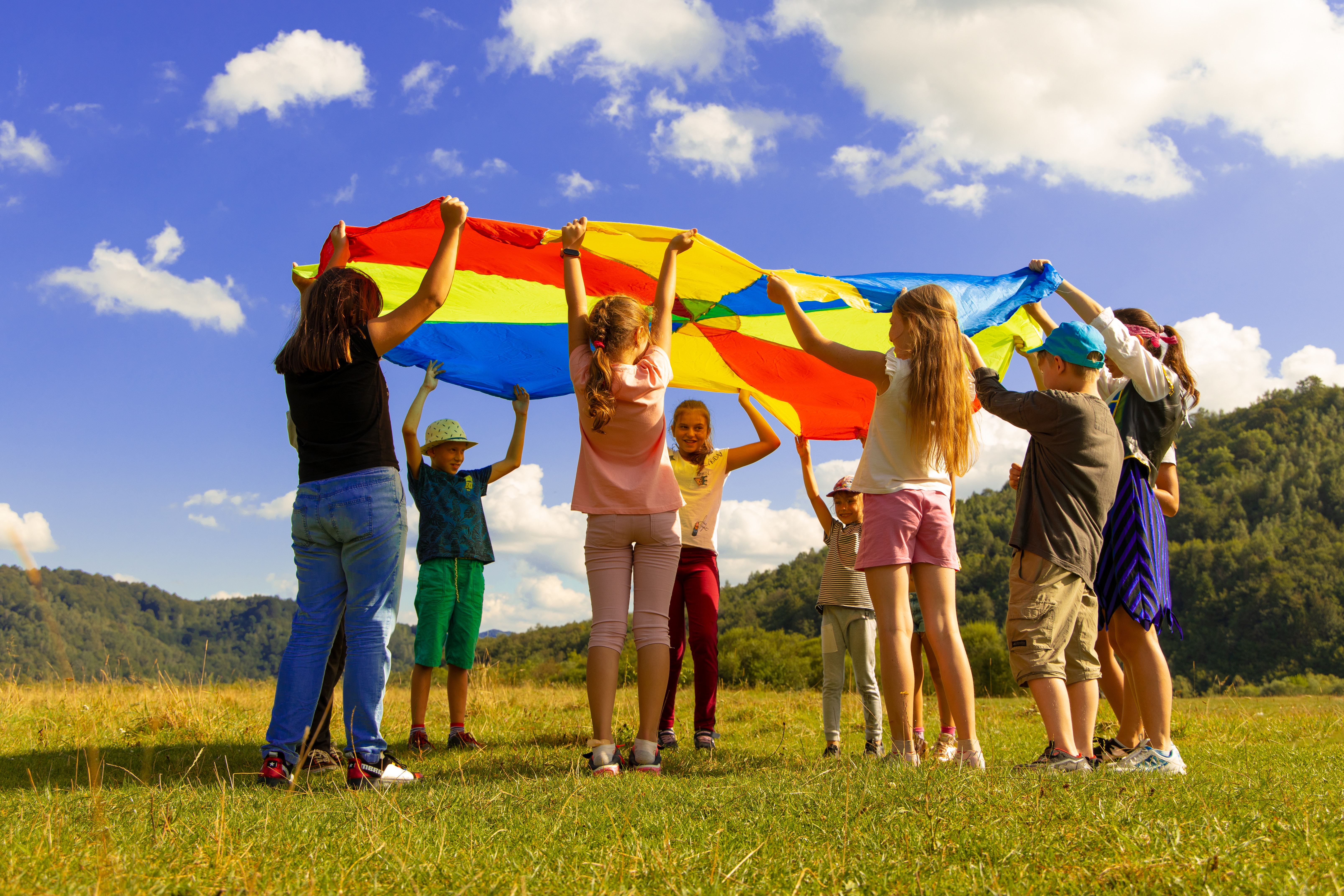 A group of children in a circle with a rainbow parachute