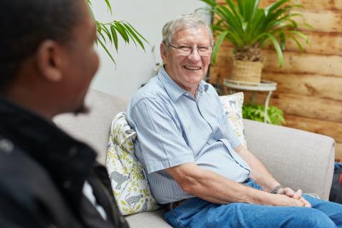 Older man sitting down, smiling whilst talking to another person