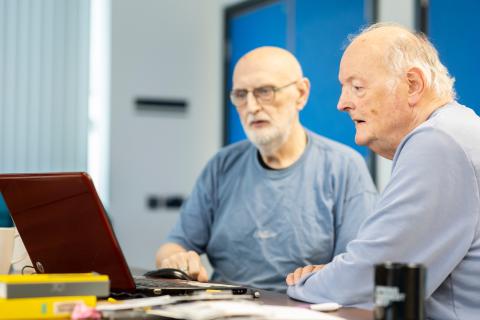 Two older gentlemen sat next to each other looking at a laptop screen