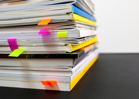 A pile of books stacked on top of each other, coloured tabs inside some of the books.